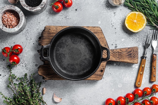 Various organic spices herbs and ingredients around empty aged cooking skillet Gray background Top view Copy space