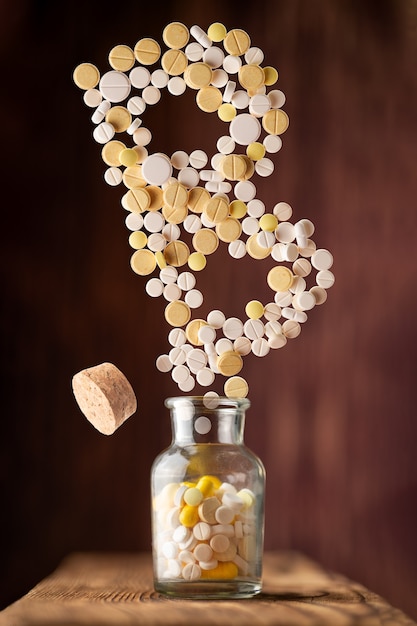 Various pills fly out of a glass jar in the form of letter B on a wooden background