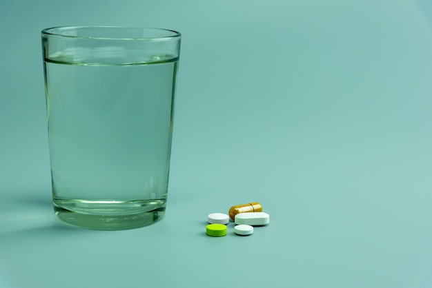  various pills and glass of water on gray background