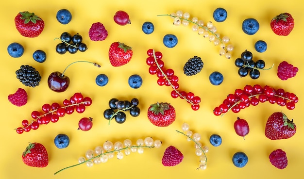 Various ripe fresh summer berries on a yellow background