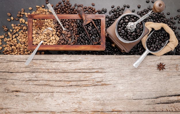 Various of roasted coffee beans in wooden box with manual coffee grinder setup on shabby wooden.