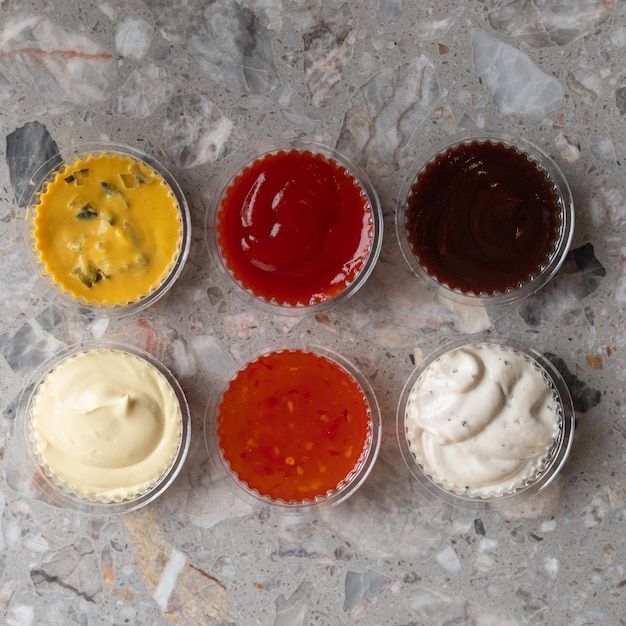 Various sauces and dips in plastic bowls on gray stone background Copy space