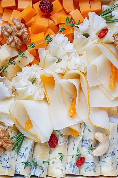 Various sorts of cheese layed out on a plate, decorated with berries, nuts and herbs, top view