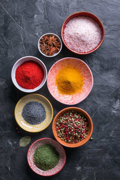 Various spices in bowls on black stone