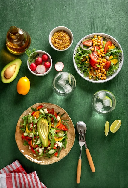 Various summer healthy vegetables salads with avocado, cucumber, radish, bell pepper and tomato on green background. Healthy food.Top view.