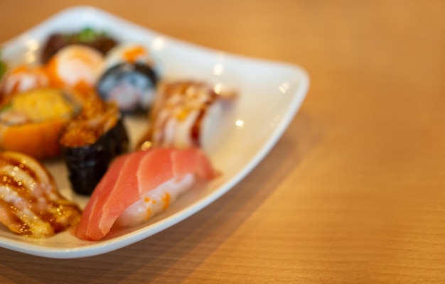 Various sushi in a white plate placed on a wooden table