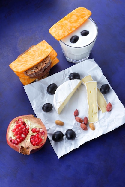 Various types of cheese composition on a blue background closeup Cheeses with fruits nuts and a glass of milk on parchment paper