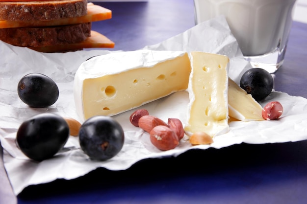 Various types of cheese composition on a blue background closeup Cheeses with fruits nuts and a glass of milk on parchment paper