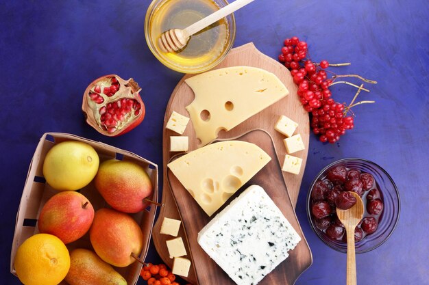 Various types of cheese composition with honey and apples in a wooden basket on a blue background Cheeses with fruits and berries on wooden boards Closeup