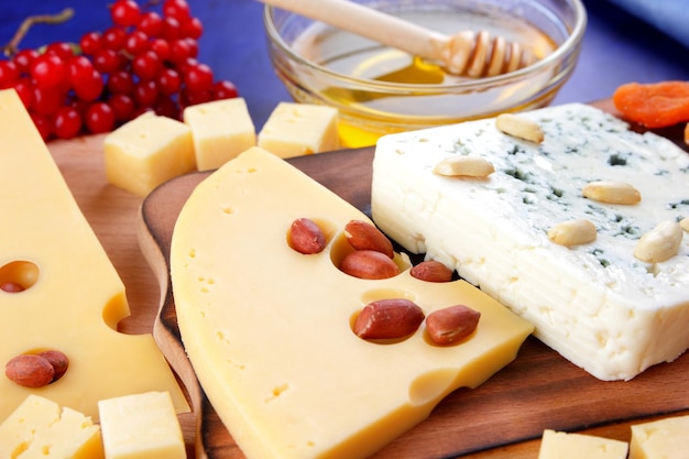 Various types of cheese composition with honey bread rolls and a blue napkin on a blue background Two types of cheese with fruits berries nuts and dried fruits on a wooden board