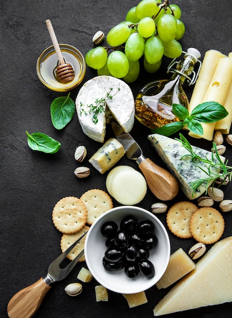 Photo various types of cheese grapes honey and snacks on a black concrete background