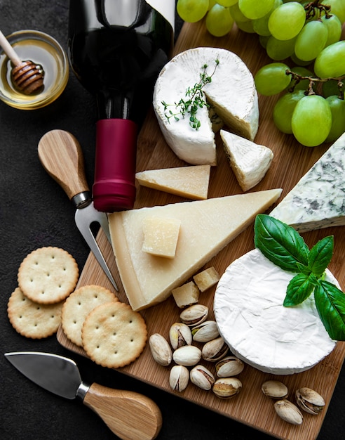 Various types of cheese, grapes and wine on a black concrete surface