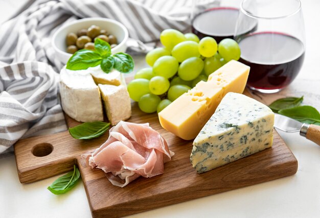 Various types of cheese, grapes, wine and snacks on a white marble background