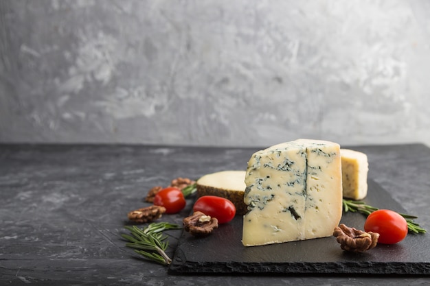 Various types of cheese and tomatoes on black board on a black background