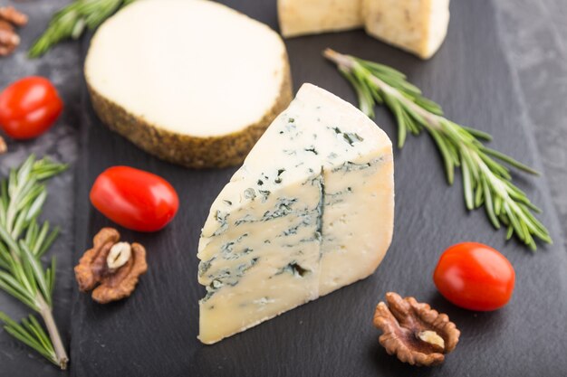 Various types of cheese with tomatoes on black board on a black background