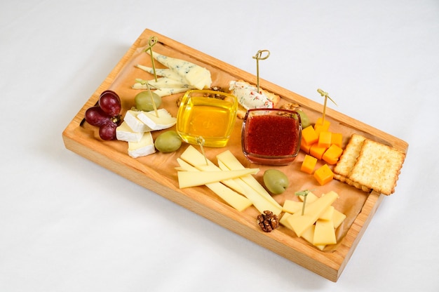 Various types of cheese on wooden cutting board, top view.