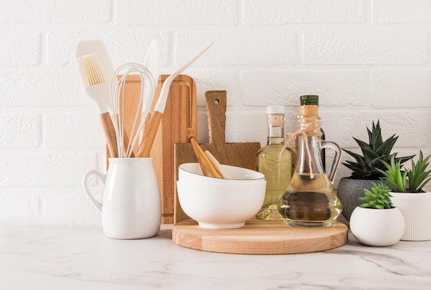 Various types of kitchen utensils and oil bottles on the marble countertop opposite the white brick wall the concept of home kitchen decor