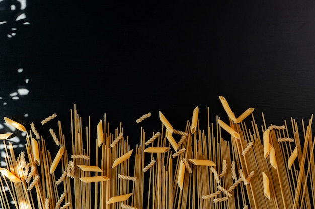 Various types of pasta on a black concrete background