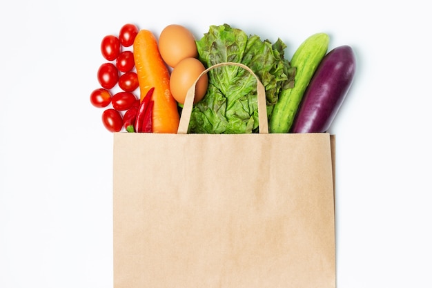 Various vegetables and fruits in a paper bag on a white surface