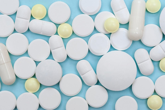 Various white pills closeup on a blue background flat lay