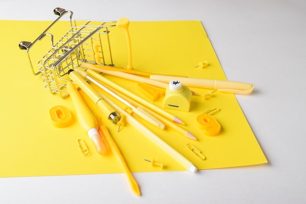 Various yellow stationery items are lying in a supermarket cart on a yellow background Back to school