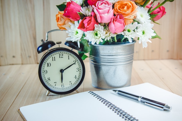 Vase bouquet Roses near black vintage clock and notebook