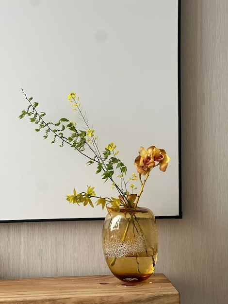 A vase of flowers is on a table with a black frame behind it.