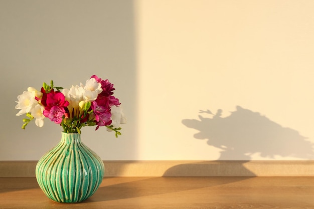 Vase with beautiful freesia flowers on floor