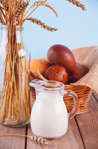 Vase with a bouquet of wheat stems, jar of milk and basket with bread  