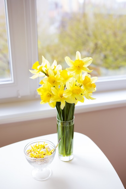 Vase with bright yellow daffodils on white wooden table