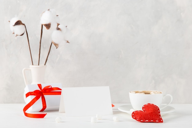 A vase with cotton, red heart, morning coffee and a gift against the of a light wall, concept, a postcard for Valentine's Day.