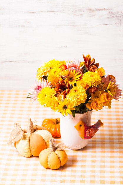 Vase with flowers and small orange textile pumpkins on a table