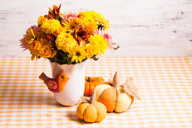 Vase with flowers and small orange textile pumpkins on a table