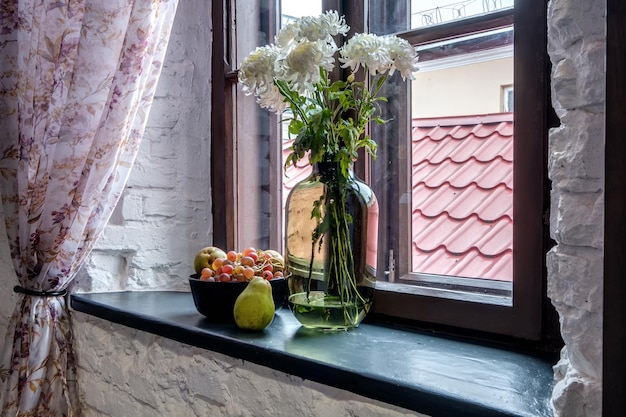 Vase with flowers on windowsill in old vintage style with fruits or candles