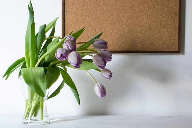 Vase with purple tulip flowers and wooden board. Copy space