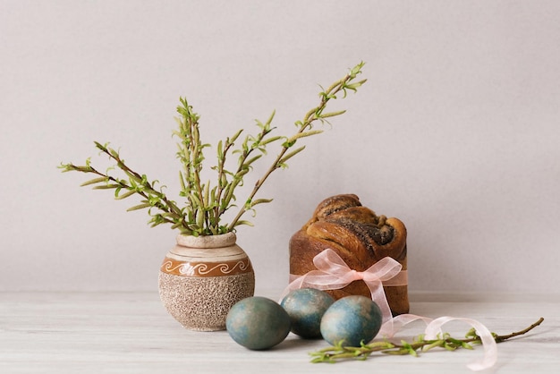 Photo a vase with a spring branch and an easter cake, painted with eggs on the table