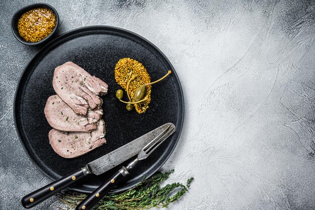 Veal or beef boiled tongue slices on a plate. White background. Top view. Copy space.