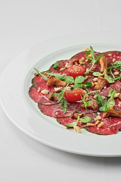 Veal carpaccio with spices and oil on a white plate on a white tablecloth Closeup selective focus