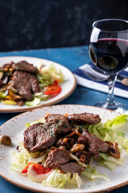 Veal salad with fresh vegetables on a plate served with red wine