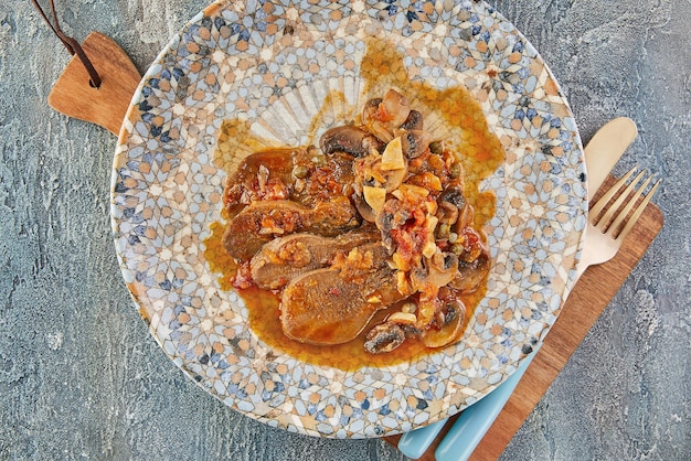 Veal tongue with tomato sauce, mushrooms and capers. French gourmet cuisine