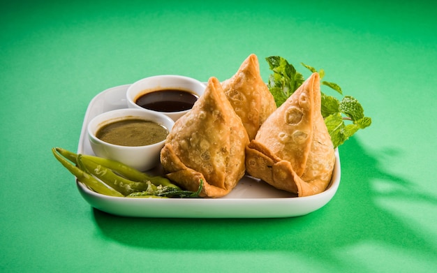 Veg Samosa is an Indian popular snack or junk food Served with fried green chilly, onion & chutney or ketchup