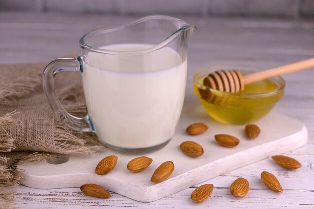 Vegan almond milk in a glass carafe on a white wooden background.