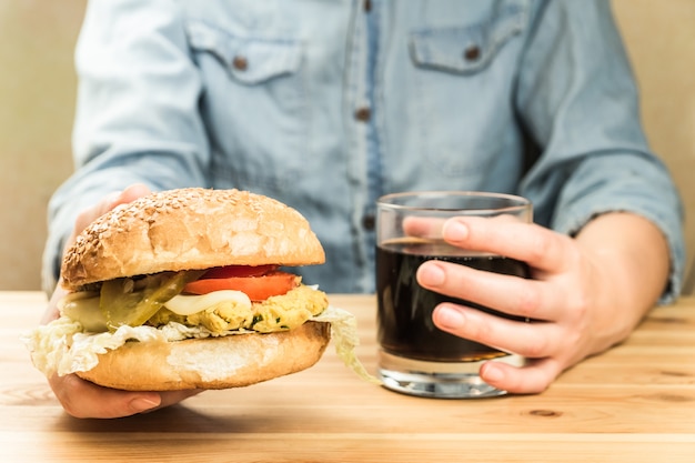 Vegan burger and glass of soft drink in hands