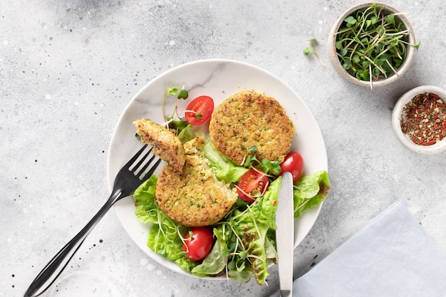 Vegan burgers with quinoa, broccoli and salad in plates on light marble background