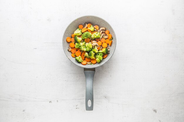 Vegan ceramic pan. Vegetarian food - broccoli carrot mushrooms salt pepper on butter.