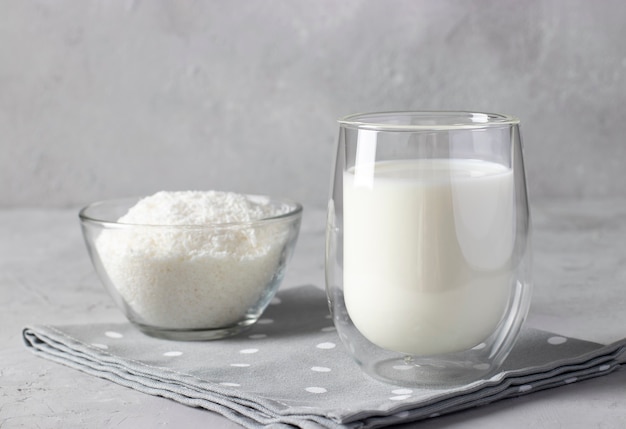 Vegan coconut milk made from coconut flakes in a transparent glass on light gray background. Making coconut milk at home