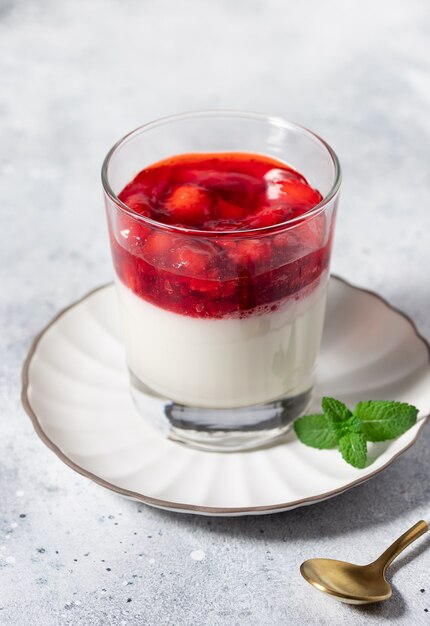 Vegan coconut panna cotta with strawberries in glass on gray background