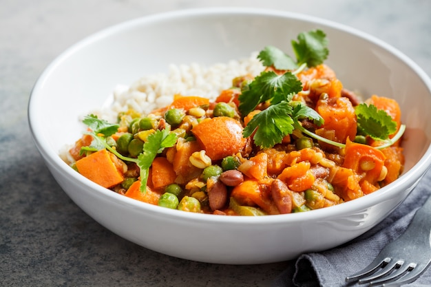 Vegan curry with rice in white bowl. Curry with sweet potato, peas and beans in a plate with rice.