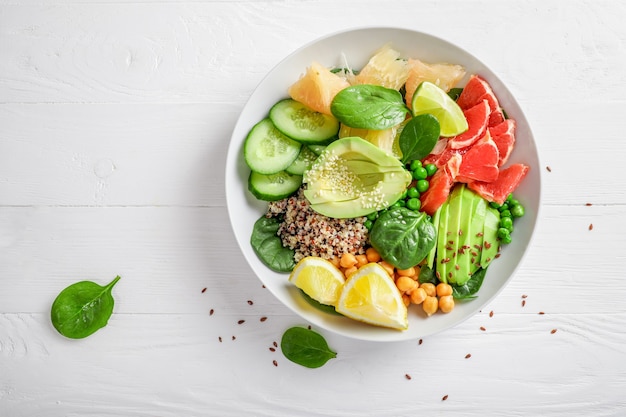 Vegan food concept: quinoa with avocado, cucumbers, green peas, chickpeas, spinach and citrus fruits on white background. Top view.