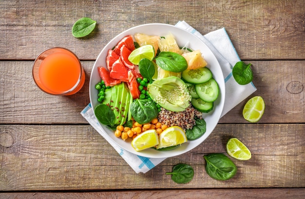 Vegan food concept: quinoa with avocado, cucumbers, green peas, chickpeas, spinach and citrus fruits on wooden background.